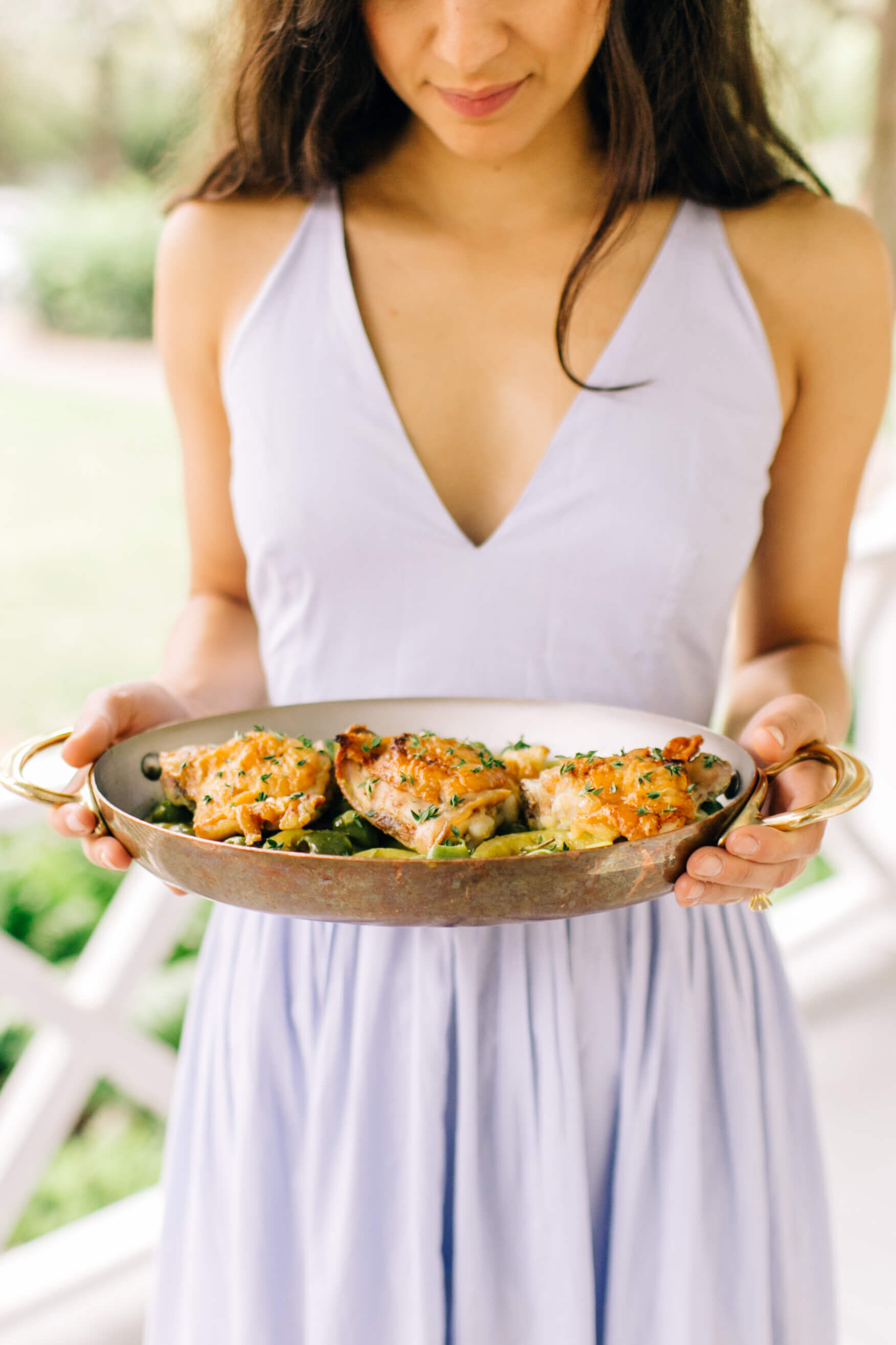 Person in lavendar dress holding a pan of Braised Chicken Thighs, with olives lemon, and thyme.