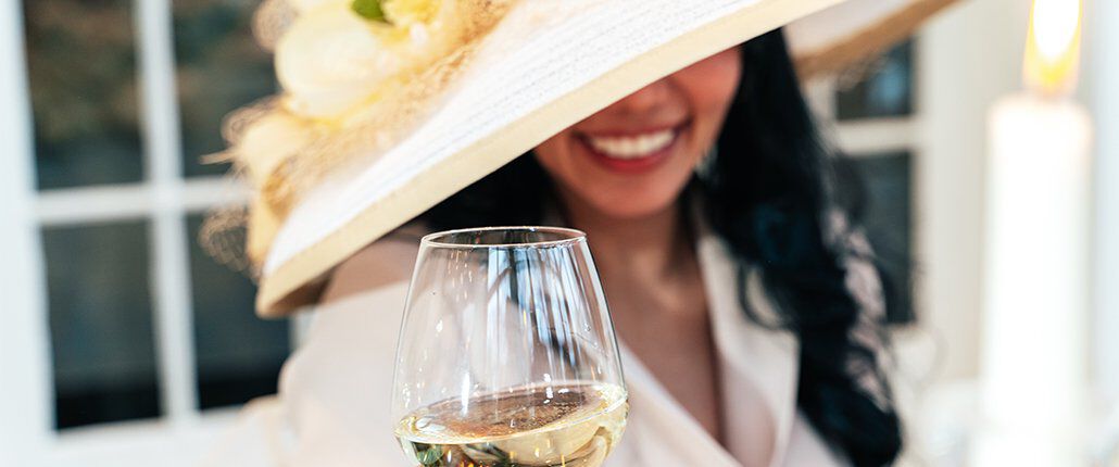 A person with an ornate hat with a glass of white wine