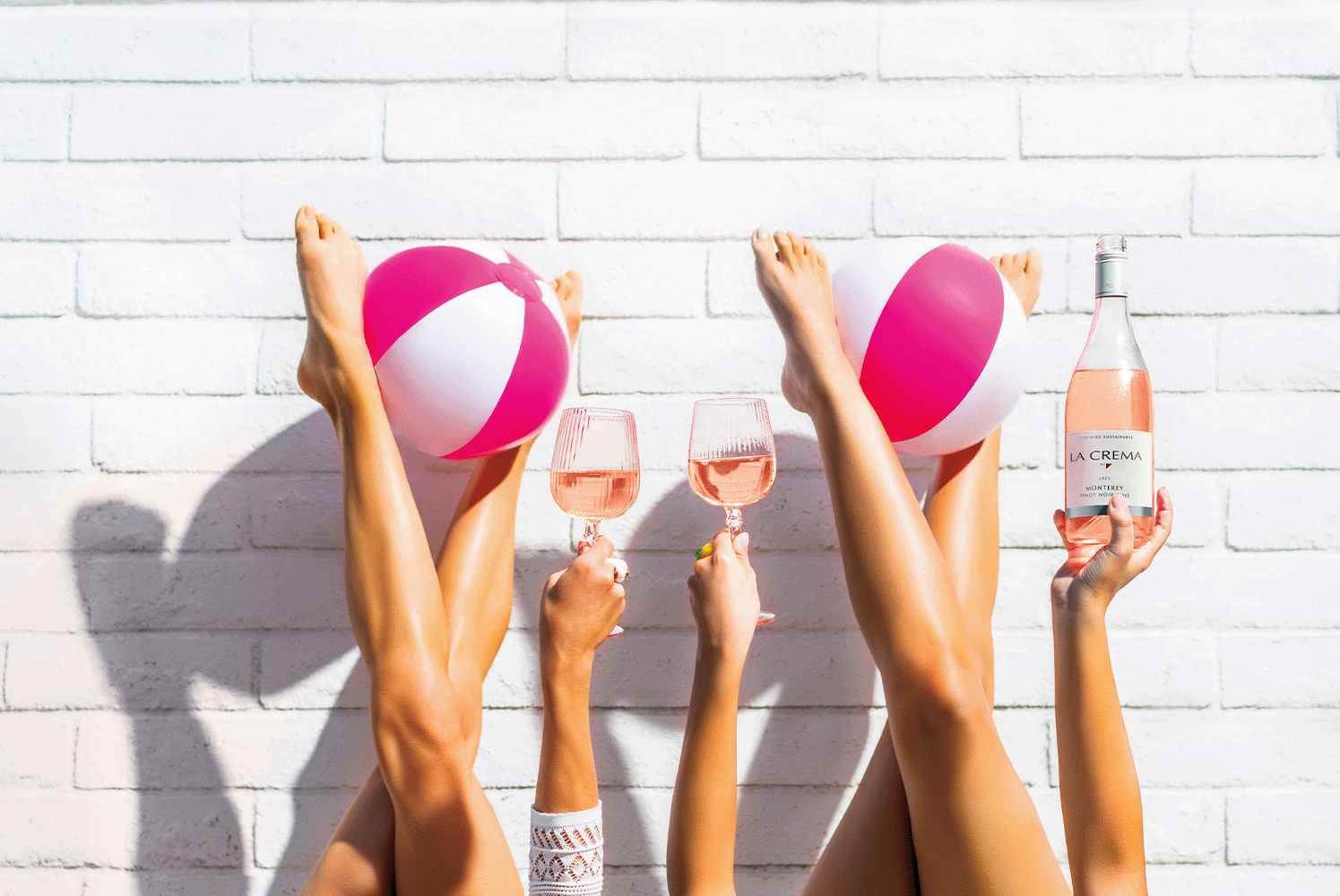 Lifestyle photography of friends with glasses of Monterey Rose and pink beach balls.  The La Crema Rose of Pinot Noir is featued as a premium summer wine choice.