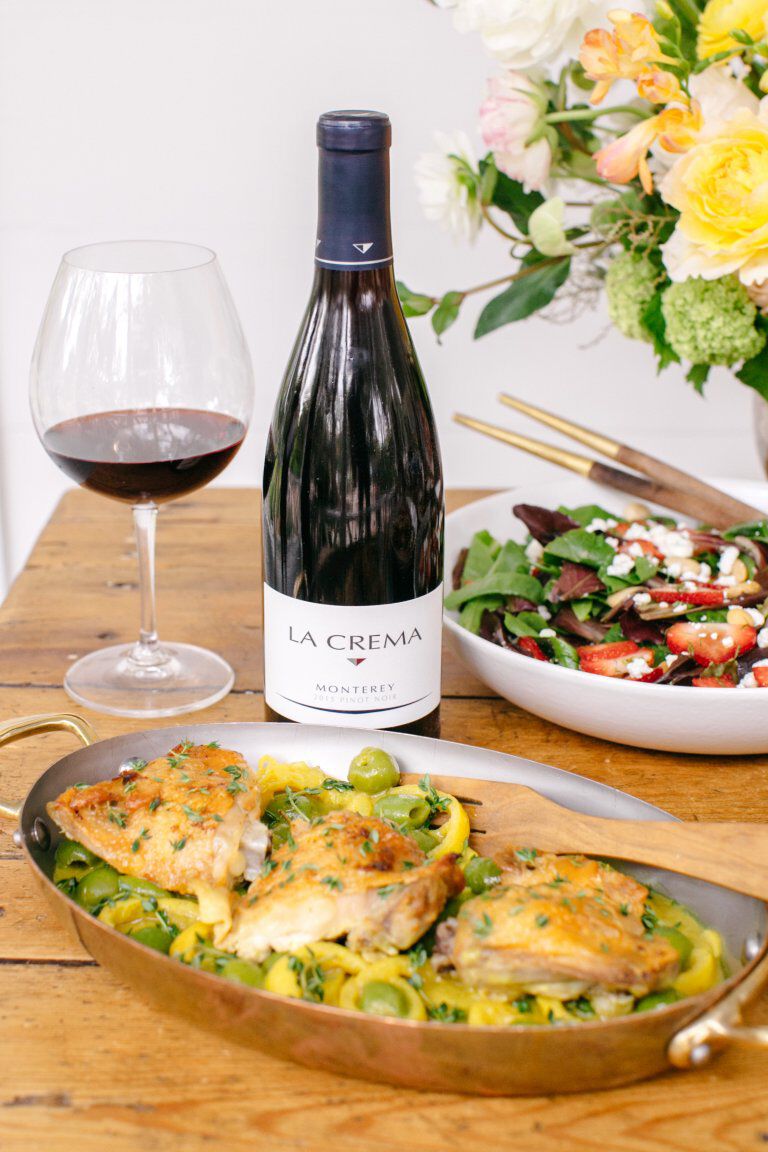 A bottle of La Crema Monterey Pinot Noir on a table with a pen of braised chicken thighs with olives, lemon, and thyme.