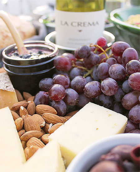 A cheese tray featuring a variety of fresh local cheeses, almonds, olives, red grapes, homemade preserves and crackers